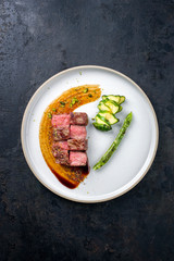 Barbecue dry aged wagyu fillet steak on hot smoked sauce with grilled green asparagus and sliced zucchini as top view on a modern design plate with copy space