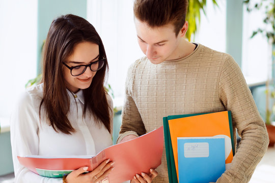 Two hard-working students discussing some matter standing in corridor holding some folders and learning materials in hands