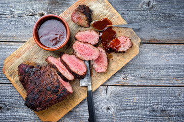 Barbecue dry aged wagyu tri tip steak with BBQ sauce as dip as top view on a wooden cutting board...