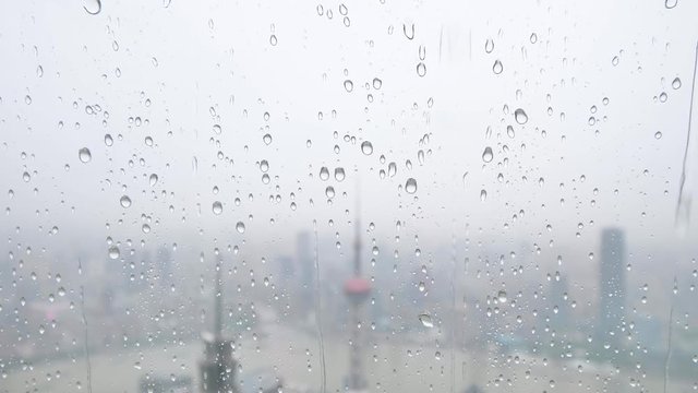 Rain water drops falling on windows glass in summer, slow motion, 4k footage, heavy rain fall with Shanghai Bund landmarks background.
