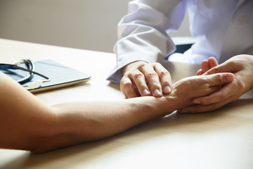 Doctor holding patient hand and examing pulse rate in medical office.