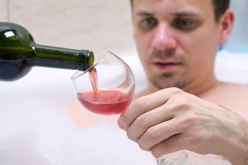 Adult man pour red wine from bottle to wine glass at home in the evening closeup.