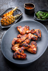 Exotically barbecue chicken wings with hot chili sauce, jalapeno and pineapple as top view on a cast iron plate