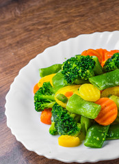 Mixed vegetables. green bean, broccoli and carrots in white plate on a wooden table background. 