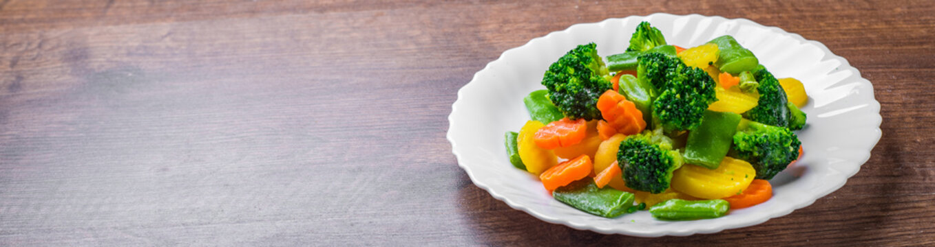 Mixed vegetables. green bean, broccoli and carrots in white plate on a wooden table background. 