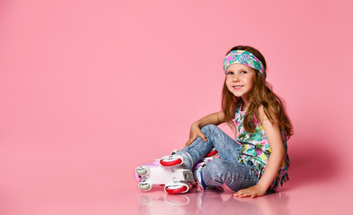 Little baby blond hair child sitting with roller skates in a white shirt and hairband happy smile...