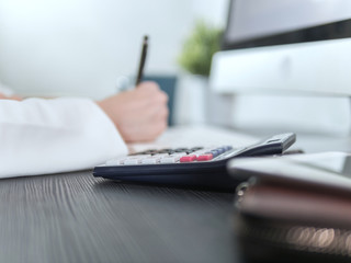Calculator on table with blurred businesswoman writing for accounting or financial concept.