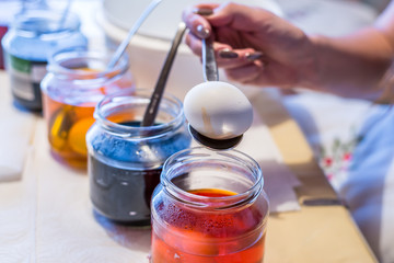 Junge Frau färbt Ostereier Zuhause in der Küche im Gurkenglas und mit verschiedenen Farben, Deutschland