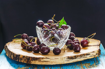 sweet cherry in a crystal vase on a birch board on a black background with a green leaf