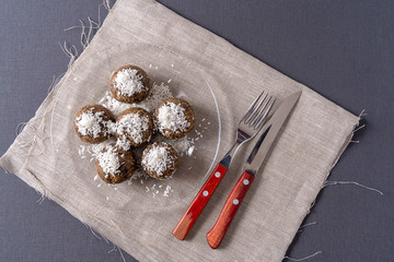 Healthy organic energy balls made with dates, prunes, raisins, peanut, with coconut shavings, in a glass plate on gray background.
