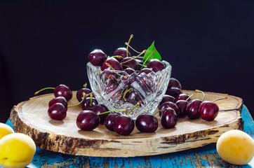 sweet cherry in a crystal vase on a birch board on a black background with a green leaf