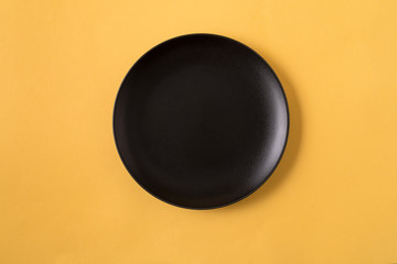Food background with empty black plate, over yellow background, flat lay.