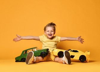 Kid boy in yellow t-shirt and shorts sitting with big sport car toys as birthday present with hands...
