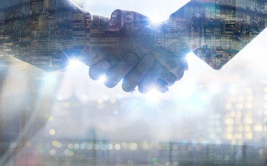 Two business people shaking hands as symbol of agreement, consolidation, business development and support. Multiple exposure image