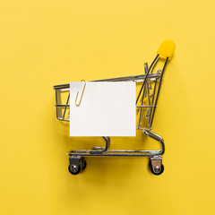 Shopping cart and white paper note list over yellow background. Shopping concept on bright yellow...