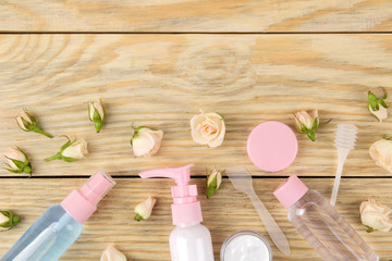 Face and body cosmetics in pink bottles with fresh roses on a natural wooden background. creams and lotion. spa. top view. space for your text