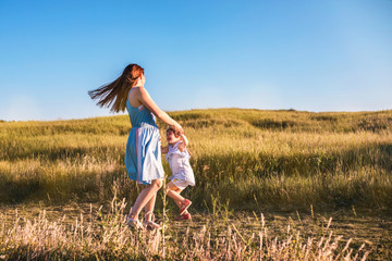 Young mother and daughter dancing and playing in a golden field of sunshine. - obrazy, fototapety, plakaty
