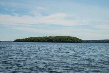 Fototapeta premium Sunny day in rice lake, Canada with blue sky and white clouds and an island on the other side of water. 