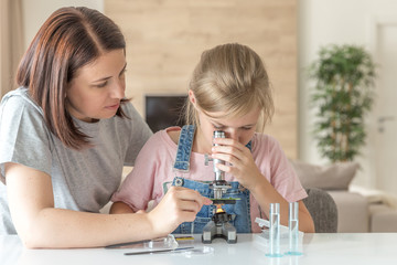 Mother and young daughter doing some experiments with microscope at home