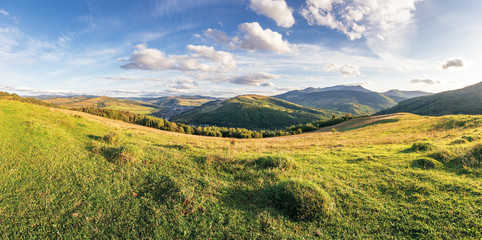 panorama of a countryside in mountains. beautiful early autumn landscape in evening light. grassy meadow on the hill. fluffy clouds above the distant ridge. village down in the valley