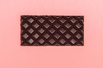 Brown chocolate bar on pink background. Copy space