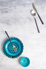 Turkish ceramics decorated blue plate and bowl with new luxury black cutlery on stone background, top view