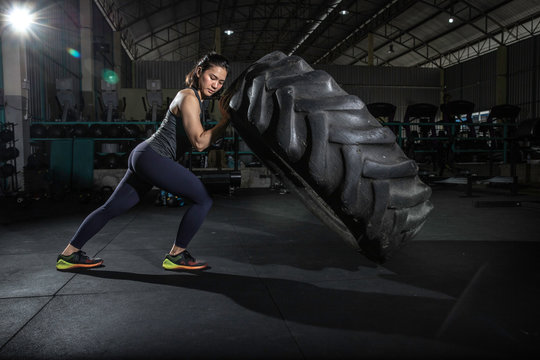 Powerful, attractive muscular girl engaged in crossfit, training with giant tires in the gym. The athlete pushes a large wheel. Exercise with heavy weight in the gym.