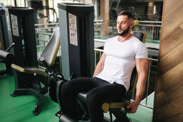 Fototapeta na wymiar Man trains legs in gym. Handsome bearded bodybuilder training