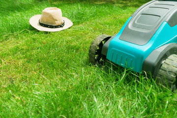  Lawn mower mowing green grass and a sunhat. Summer work in the garden.