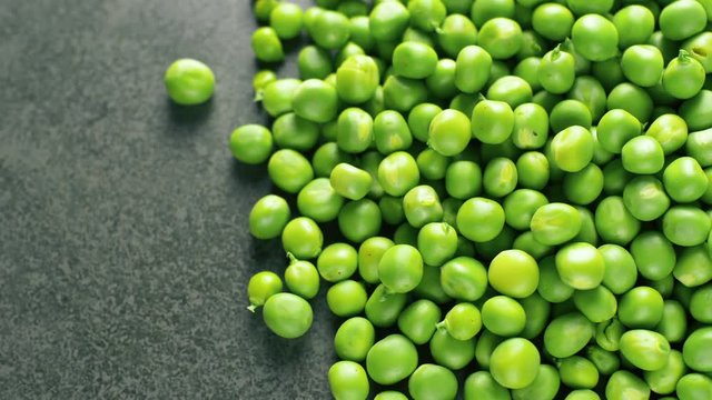 Fresh green pease rotating on dark texyure surface. Close up 4k footage.