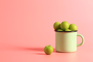 green cherry plum in an enamel mug on a pink background. Creative minimalist style. healthy food