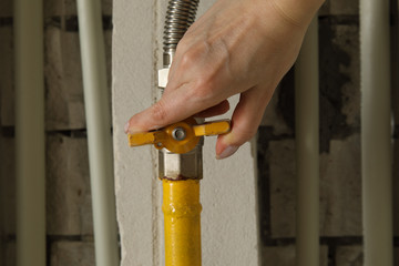 Woman turning on or turning off gas supply on yellow gas pipe