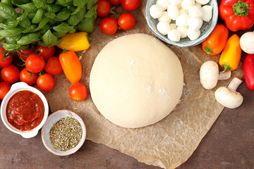 Raw dough for pizza with ingredients and spices on table