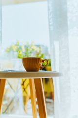 Yellow cup with hot drink on the table against the background of flowers