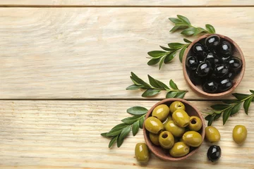 Foto op Plexiglas Green and black olives in a wooden bowl with leaves on a natural wooden table. top view. space for text © MK studio