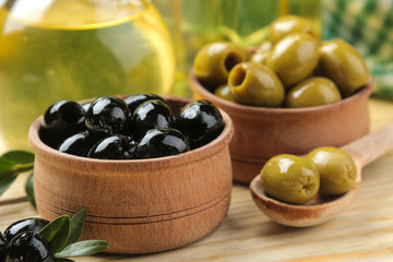 Green and black olives in a wooden bowl with leaves and olive oil on a natural wooden table. close-up