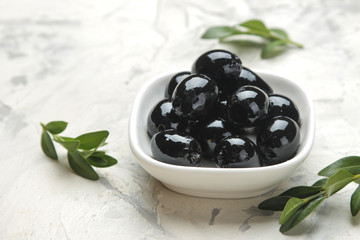 black olives in a white ceramic bowl with leaves on a light concrete background. close-up
