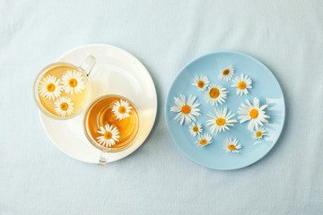 Herbal tea with fresh chamomile flowers in glass teacup on blue plate, seasonal colds flu alternative treatment, antidepressant and a remedy stomach cramps