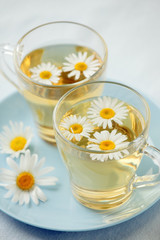 Herbal tea with fresh chamomile flowers in glass teacup on blue plate, seasonal colds flu alternative treatment, antidepressant and a remedy stomach cramps
