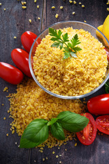 Bowl of uncooked bulgur on wooden table