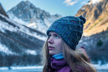 portrait of a beautiful young woman in front of snow covered mountains and frozen lake during cold autumn day in Caucasus mountains, Russia