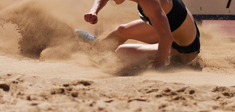 Female athlete long jump landing sand spray