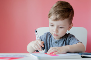 Portrait of cute kid boy at home making homework. Little concentrated child writing with colorful pencil, indoors. Elementary school and education. Kid learning writing letters and numbers