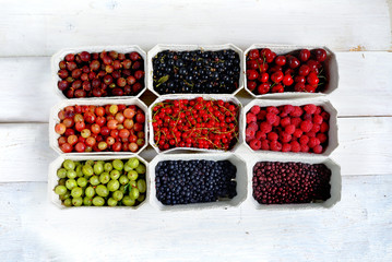 Healthy summer fruit variety. Sweet cherries, strawberries, blackberries, gooseberries, red currant and black currant in paper boxes over a rustic wooden background. Top view