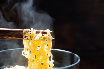Chopsticks to tasty noodles with steam and smoke in bowl on wooden background, selective focus.,...