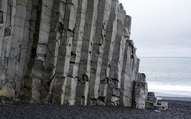 Close up of geometric formations of volcanic rock on Iceland. The Rock on the Atlantic coast  rises from a black sand beach with the ocean and blue sky in background