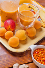 fresh fruit smoothie with banana and apricots at orange  tray  with blender  at wooden table. close up