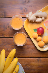 fresh fruit smoothie with banana and apricots at orange  tray  with blender  at wooden table. flat lay