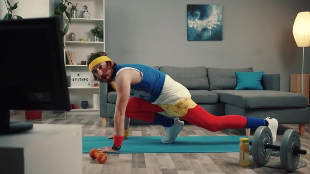 Handsome concentrated sportsman in retro outfit training abs at home. Motivated athlete man trying to get fit exercising on mat and watching sport videos.