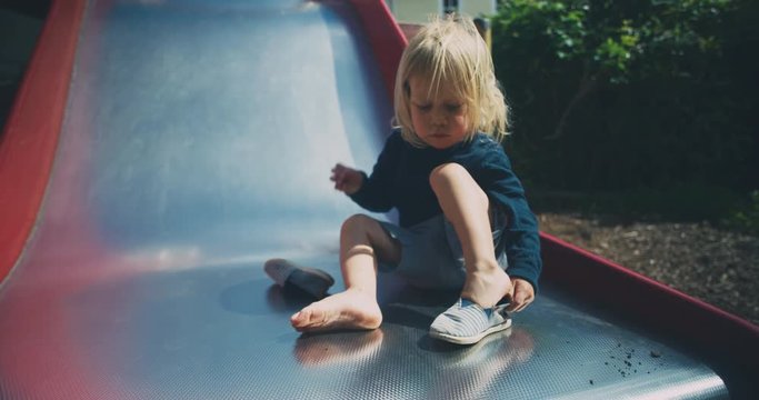 Little toddler sitting on slide and putting on his shoes